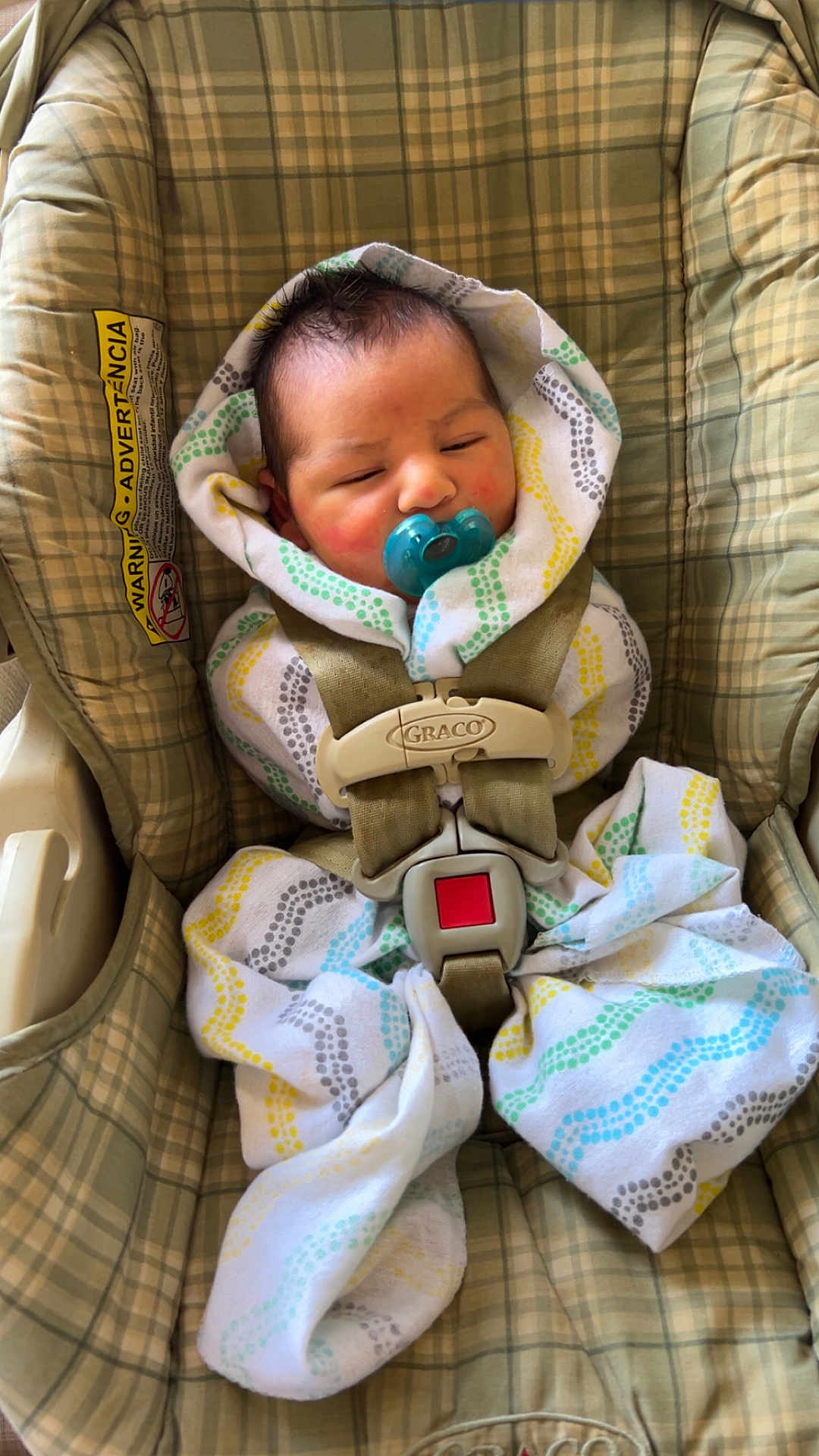 Angel is registered to the contest to win money with this photo: baby, infant, car_seat, pacifier, swaddle, patterned_cloth, plaid, safety_harness, child, face, head, sleepy, indoors, seatbelt, cute, newborn, comfort, resting, young_child, fabric