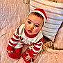 baby, beige, child, couch, cozy, cute, face, festive, holiday, indoors, infant, looking_up, pillow, portrait, red_hat, red_socks, sitting, soft_texture, striped_sweater, warm_colors
