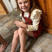 Brooklyn is registered to the contest to win money with this photo: child, girl, smiling, barefoot, sitting, floor, tiles, sandals, orange, hair_tied, long_hair, white_shirt, dress, indoor, wood_paneling, door, happy, casual, hands_together, young