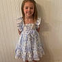 Brooklyn is registered to the contest to win money with this photo: child, girl, smiling, dress, floral, indoor, wood_floor, wall, white_wall, standing, footwear, sandals, happy, young, person, fashion, casual, portrait, cute, front_view
