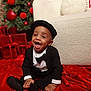 baby, child, tuxedo, hat, smile, red_velvet, christmas_tree, ornaments, presents, couch, holiday, festive, indoor, celebration, joyful, sitting, black_clothing, cute, portrait, happy