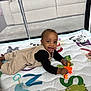 baby, child, playpen, play_mat, toy, smiling, indoor, couch, mesh, clothing, person, happy, lying_down, infant, colorful, black_shirt, beige_outfit, bright_toy, curious, young_child