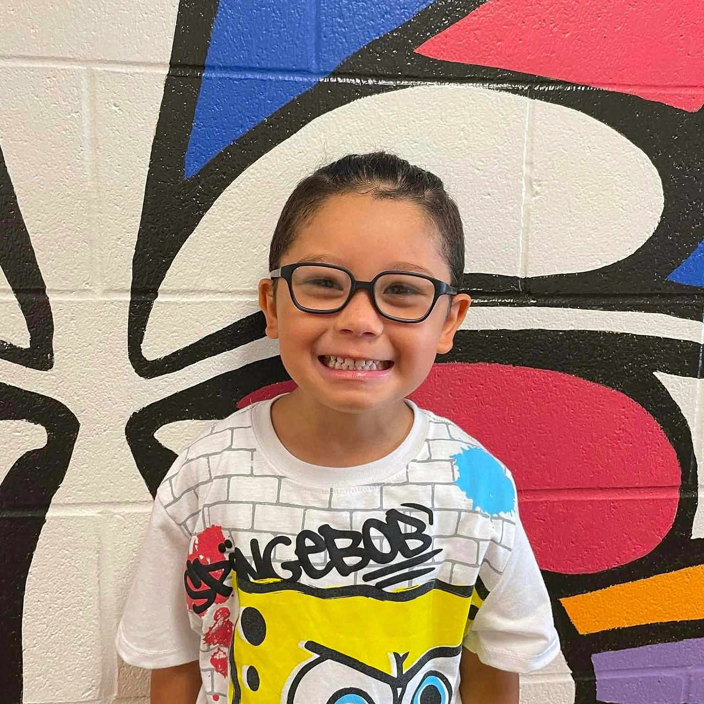 Ta'Vion is registered to the contest to win money with this photo: art, boy, casual, child, colorful, fashion, glasses, graffiti, graphic_tshirt, happy, indoor, person, portrait, short_hair, smiling, spongebob, standing, tshirt, wall, youth