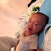 Troy is registered to the contest to win money with this photo: baby, infant, bed, blanket, pillow, striped_clothing, onesie, face, expression, yawning, hand, wicker_basket, wall, indoor, person, sleepwear, resting, closeup, head, cozy
