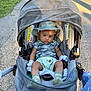 Troy is registered to the contest to win money with this photo: baby, stroller, hat, baby_clothing, camouflage, outdoor, pathway, sunlight, mesh_cover, baby_socks, baby_gloves, greenery, sidewalk, baby_face, infant, baby_seat, baby_accessories, child, summer_clothing, shadows