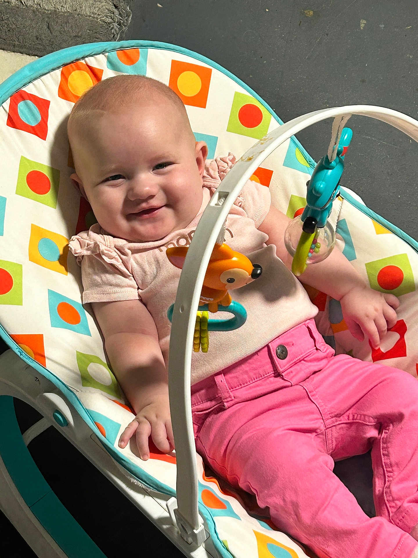 Isabella joined the competition — help win amazing prizes! baby, smiling, pink_pants, baby_rocker, toys, colorful, indoor, child, cute, happy, infant, clothing, play, face, person, seat, relaxing, casual, childhood, comfort