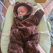 David joined the competition — help win amazing prizes! baby, sleeping, pacifier, brown_onesie, hood, baby_rocker, frog_design, wooden_floor, toy, infant, cozy, cute, child, soft_clothing, indoor, resting, comfort, small_face, peaceful, wearing