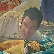 Max is registered to the contest to win money with this photo: animal, bed, blanket, casual_clothing, comfort, cozy, cute, dog, floral_pattern, friendship, home, indoor, lying_down, person, pet, portrait, pug, relaxation, resting, smiling