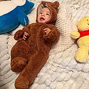 Aavani joined the competition — help win amazing prizes! baby, child, plush_toy, stuffed_animal, brown_onesie, bear_costume, smiling, cozy_blanket, white_blanket, blue_plush, yellow_toy, red_shirt, infant, cute, happy, lying_down, soft_texture, indoors, portrait, warm