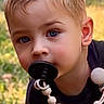 child, blonde_hair, blue_eyes, pacifier, outdoor, grass, shirt, curious, portrait, young_child, baby_accessory, cute, face, person, daylight, closeup, head, skin, expression, nature