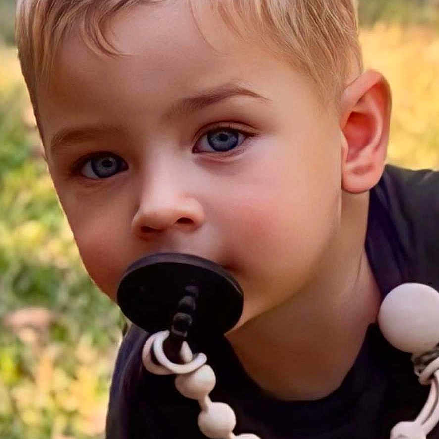 James is registered to the contest to win money with this photo: child, blonde_hair, blue_eyes, pacifier, outdoor, grass, shirt, curious, portrait, young_child, baby_accessory, cute, face, person, daylight, closeup, head, skin, expression, nature