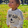 James is registered to the contest to win money with this photo: child, toddler, smiling, outdoor, grass, sunlight, sweatshirt, baby_gap, pants, cute, curious, portrait, young_child, happy, nature, daylight, fence, casual_clothing, standing, boy