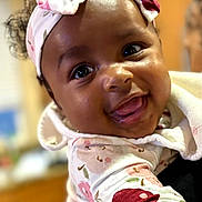 Daijah is registered to the contest to win money with this photo: baby, bow, cheeks, child, closeup, cute, expression, eyes, face, floral_pattern, happy, headband, indoor, infant, onesie, person, portrait, skin, smile, tongue_out
