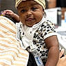 Daijah is registered to the contest to win money with this photo: arm, baby, blurred_background, child, clothing, cute, face, flower, hand, headband, holding, indoors, infant, leopard_print, onesie, people, person, portrait, skin, smile