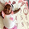 Daijah joined the competition — help win amazing prizes! arm, baby, baby_girl, blanket, bow, child, clothing, cute, happy, indoors, infant, lying_down, numbers, pink_bird, pink_headband, playful, portrait, skin, smiling, white_tank_top