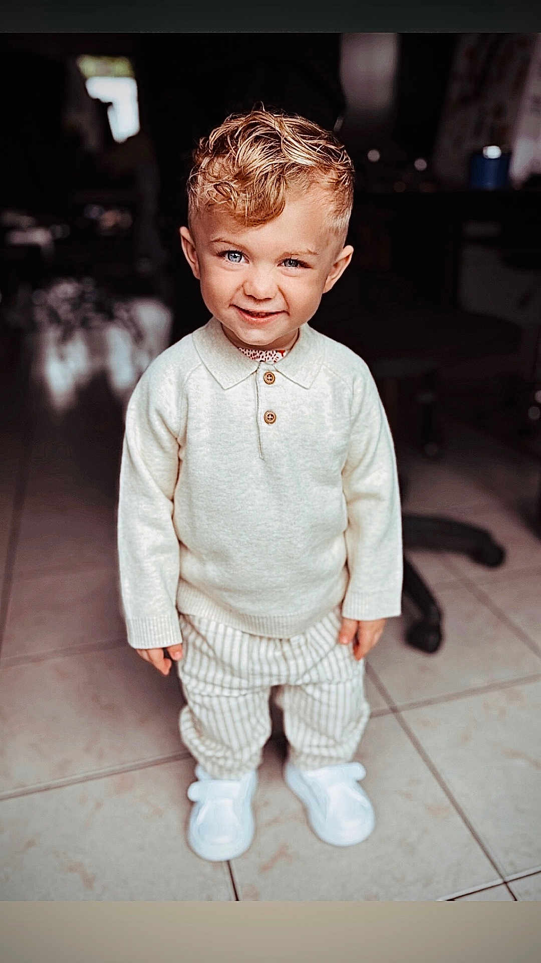 Maylone participe au concours pour gagner de l'argent avec cette photo : blond_hair, blue_eyes, boy, casual_clothing, child, curly_hair, cute, happy, indoor, person, playful, portrait, smiling, standing, striped_pants, sweater, tile_floor, toddler, white_shoes, young