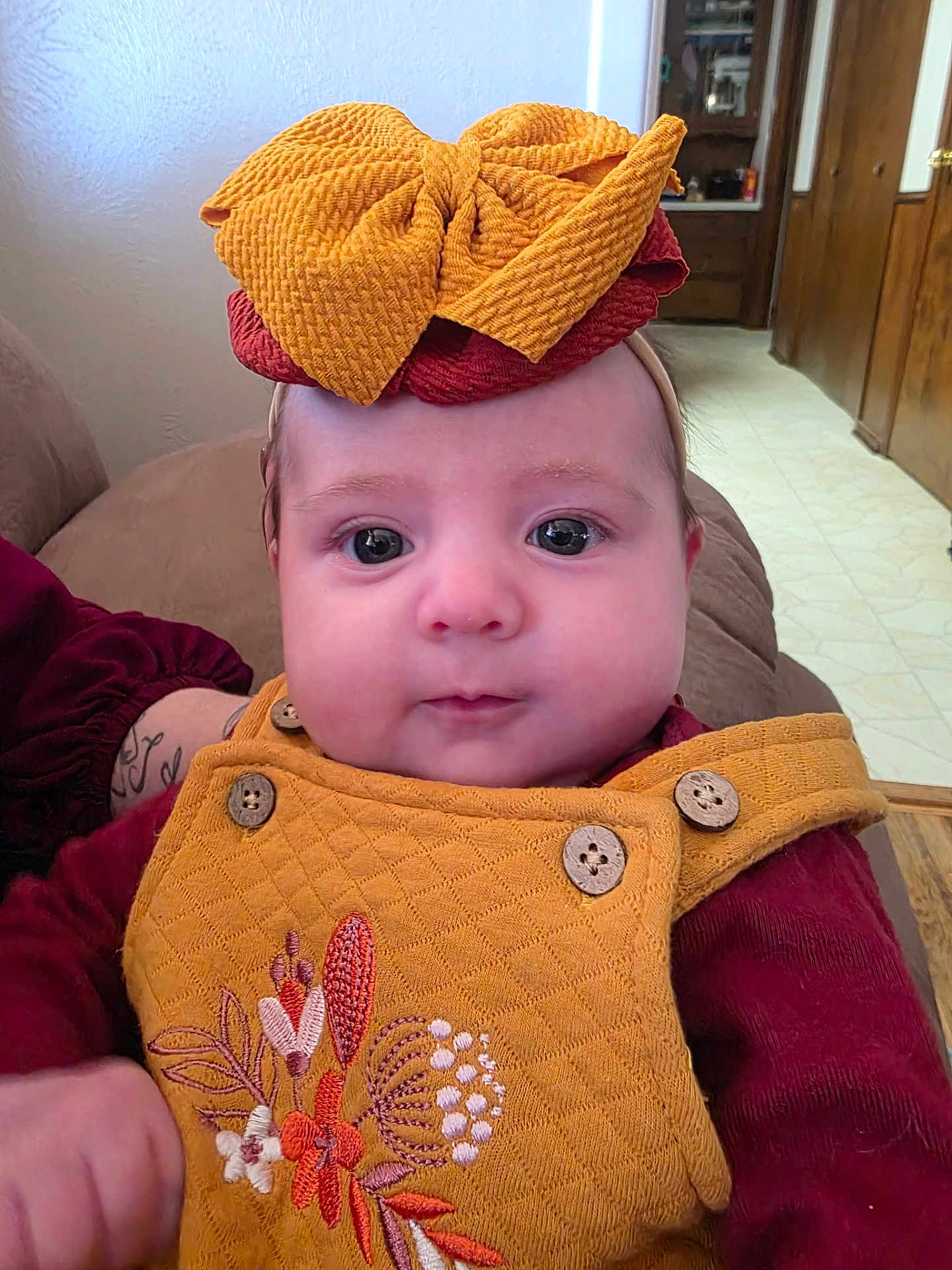 Breckilynn is registered to the contest to win money with this photo: baby, child, face, headband, yellow_clothing, embroidered, buttons, indoor, couch, furniture, person, cute, portrait, infant, expression, hand, sleeves, wall, floor, wood
