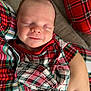 baby, newborn, infant, sleeping, smiling, face, cheek, head, plaid, pajamas, pattern, red, green, blanket, couch, arm, hand, close_up, portrait, cozy