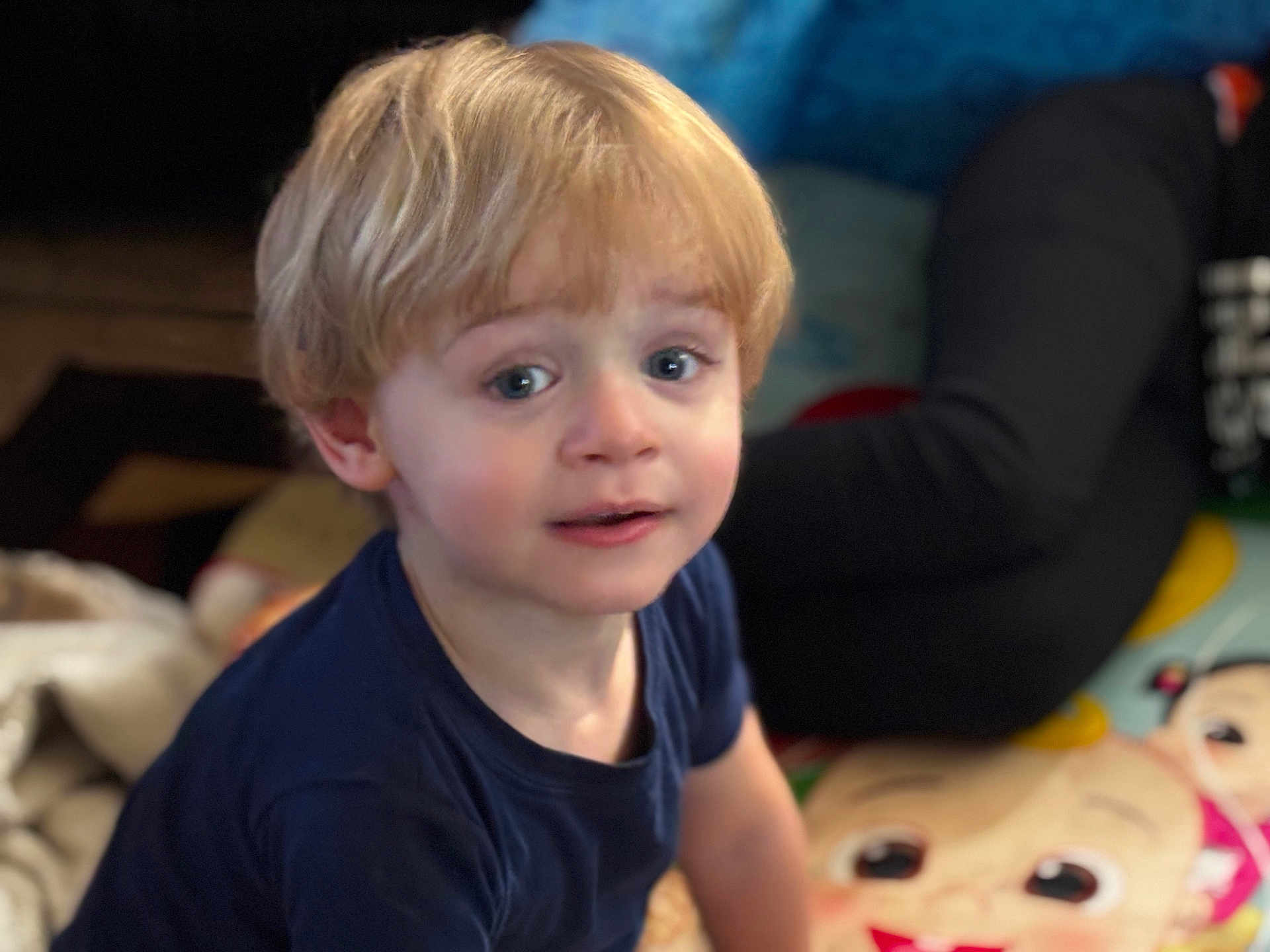 Ezekiel is registered to the contest to win money with this photo: child, toddler, blonde_hair, blue_eyes, indoor, play_mat, cartoon, blanket, person, clothing, curious, sitting, face, portrait, young_child, casual, home, expression, people, background