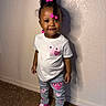 A'Moura is registered to the contest to win money with this photo: carpet, casual_clothing, child, curly_hair, cute, fashion, hair_beads, happy, indoor, jeans, person, pink_sneakers, playful, portrait, smiling, standing, toddler, wall, white_tshirt, young_child