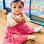 baby, child, girl, pink_dress, headband, toy, brush, floor, indoor, playpen, colorful, curious, sitting, cute, portrait, young_child, wooden_floor, happy, infant, soft_lighting