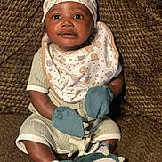 Ethan joined the competition — help win amazing prizes! baby, infant, mittens, booties, bib, hat, smile, sitting, cozy, cute, patterned, texture, brown_background, curious, child, young, portrait, clothing, indoors, soft_lighting