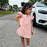 child, girl, pink_dress, hair_clips, sandals, street, suburban, car, white_suv, trees, sidewalk, curb, grass, residential_area, smiling, hair, outdoor, summer, playful, pose