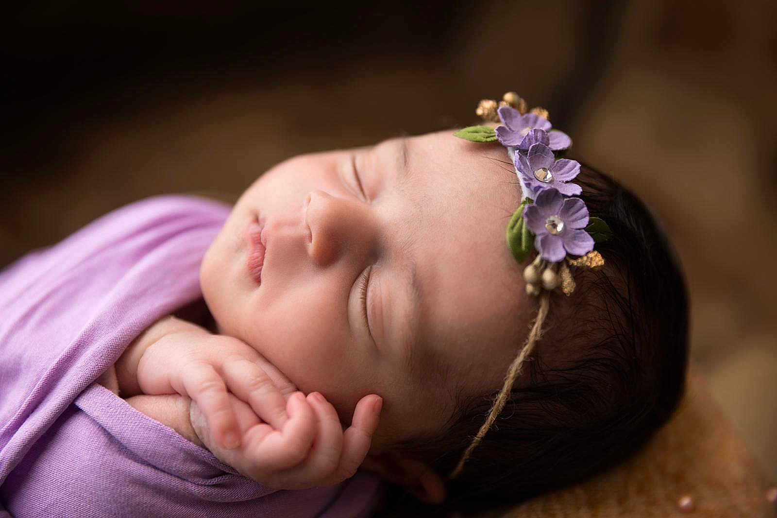 Amalyah participe au concours pour gagner de l'argent avec cette photo : newborn, baby, sleeping, flower_headband, purple_cloth, closeup, soft_light, portrait, infant, peaceful, hand, skin, face, delicate, cute, resting, indoors, warm_tones, head, child