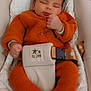 baby, sleeping, orange_clothing, knitwear, baby_seat, safety_belt, socks, indoor, infant, cute, relaxed, peaceful, child, soft_lighting, portrait, cozy, resting, head, hands, blanket