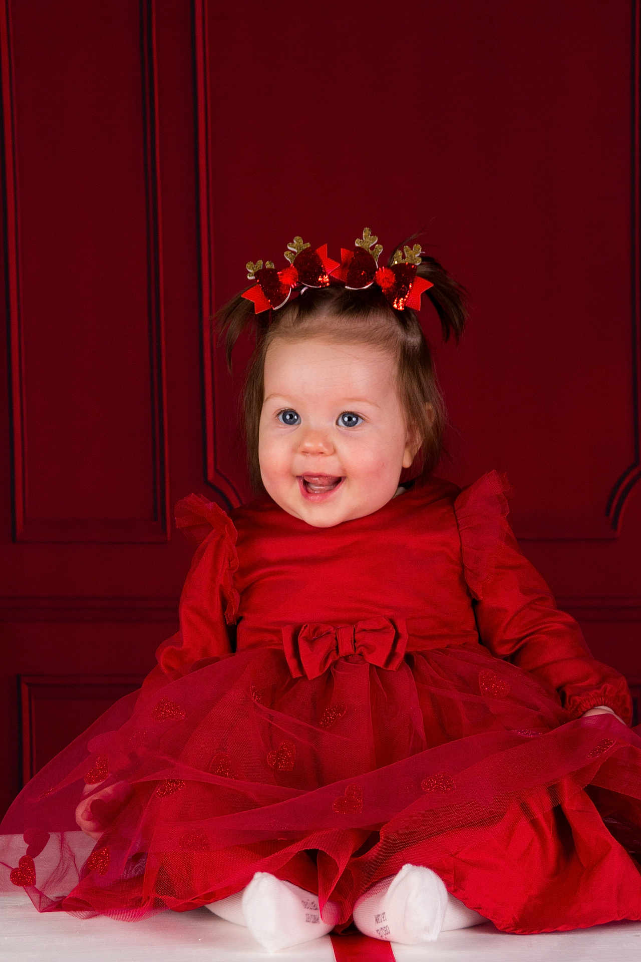 Lynaé a rejoint le concours — aidez-le/la à gagner de superbes lots ! baby, child, red_dress, headband, smiling, happy, portrait, indoor, cute, sitting, toddler, holiday, festive, heart_pattern, white_socks, girl, background, celebration, studio, adorable