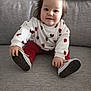toddler, child, baby, sitting, couch, gray_couch, white_sweater, red_hearts, red_pants, shoes, hair_clip, indoor, smiling, cute, portrait, young_child, clothing, happy, person, casual
