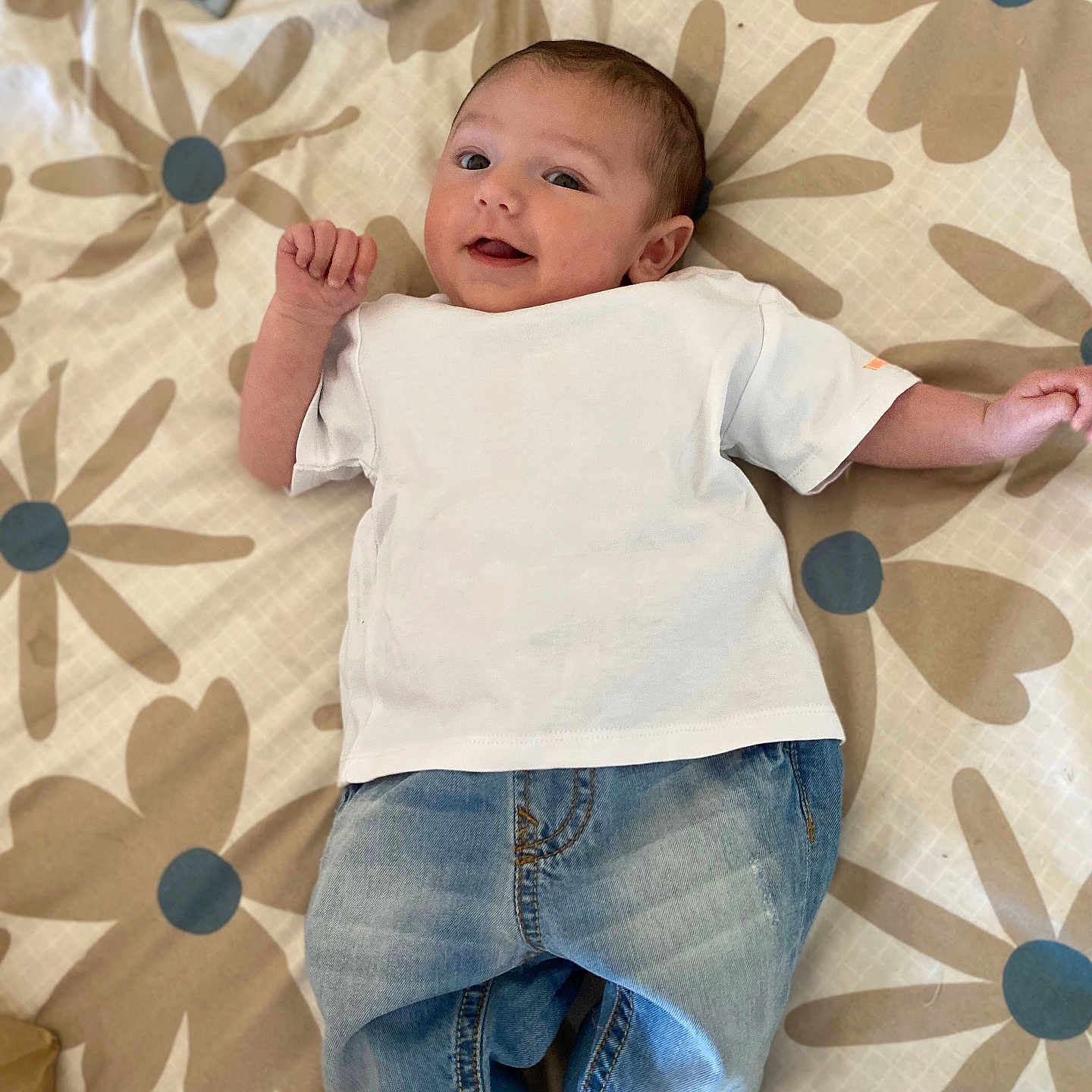 Tiago participe au concours pour gagner de l'argent avec cette photo : baby, baby_face, blanket, casual_clothes, child, comfortable, cute, denim_pants, floral_pattern, footwear, happy, indoors, infant, light, lying_down, portrait, small_hands, smiling, white_tshirt, young