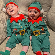 Collin And Kyler is registered to the contest to win money with this photo: baby, infant, toddler, child, elf_costume, holiday_outfit, green_hat, red_trim, couch, beige_couch, smiling, happy, cute, festive, holiday, socks, green_socks, red_socks, two_babies, indoor