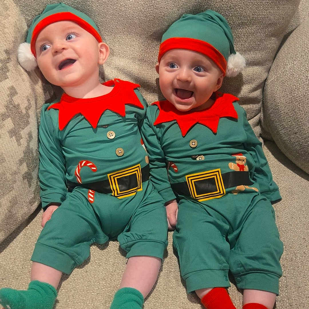 Collin And Kyler is registered to the contest to win money with this photo: baby, beige_couch, child, couch, cute, elf_costume, festive, green_hat, green_socks, happy, holiday, holiday_outfit, indoor, infant, red_socks, red_trim, smiling, socks, toddler, two_babies