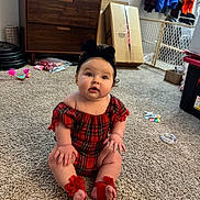 Ariya is registered to the contest to win money with this photo: baby, baby_girl, black_bow, cabinet, cardboard_box, carpet, child, curious, floor, footwear, furniture, headband, home, indoor, person, plaid_clothing, red, room, sitting, toy