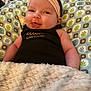 baby, infant, headband, blanket, patterned_pillow, smiling, tongue_out, cute, cozy, child, soft_texture, indoors, clothing, human, resting, face, cheeks, expression, portrait, relaxing
