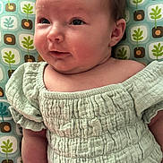 Ariya joined the competition — help win amazing prizes! baby, infant, child, face, clothing, green, patterned_background, cushion, smile, skin, arm, head, eyes, cheeks, texture, fabric, seated, indoors, cute, portrait