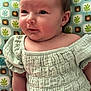 baby, infant, child, face, clothing, green, patterned_background, cushion, smile, skin, arm, head, eyes, cheeks, texture, fabric, seated, indoors, cute, portrait