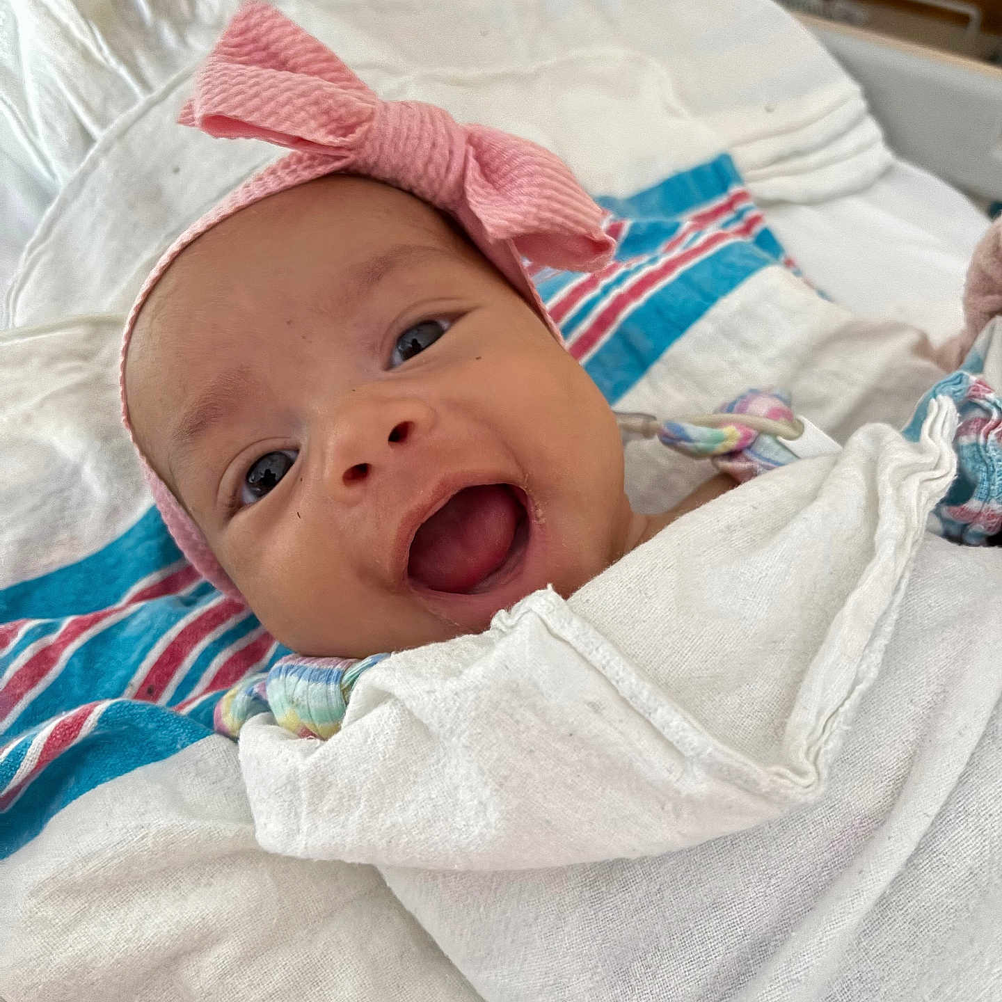 Melani Rodriguez is registered to the contest to win money with this photo: baby, blanket, closeup, colorful, cute, fabric, face, happy, headband, indoors, infant, lying_down, newborn, person, pink_bow, portrait, smiling, soft, striped, wrapped