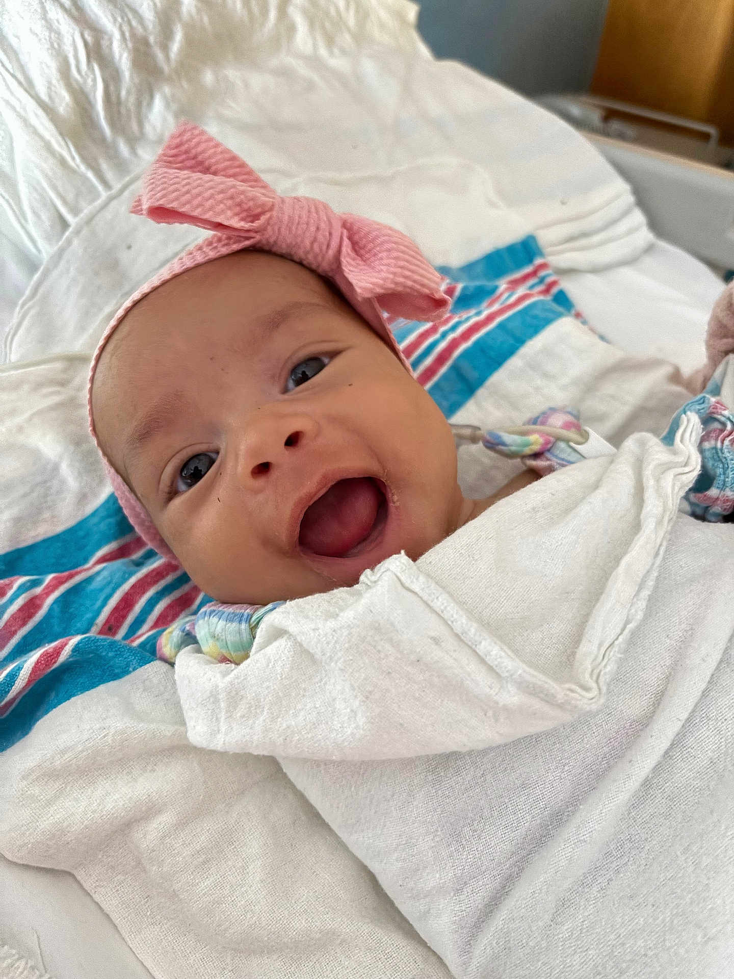 Melani Rodriguez is registered to the contest to win money with this photo: baby, smiling, headband, pink_bow, wrapped, blanket, infant, happy, face, closeup, lying_down, fabric, striped, colorful, cute, newborn, person, soft, indoors, portrait