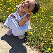 Loialti is registered to the contest to win money with this photo: child, smile, flower, white_dress, pink_shoes, sidewalk, yellow_flowers, grass, sunlight, outdoor, happy, curly_hair, nature, cute, portrait, person, daylight, flower_behind_ear, playful, greenery