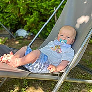 Anoa participe au concours pour gagner de l'argent avec cette photo : baby, child, pacifier, outdoor, greenery, lawn_chair, relaxing, shorts, white_shirt, dinosaur_print, sunlight, grass, summer, infant, portrait, casual, barefoot, cute, resting, nature