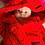 baby, child, red_robe, fluffy, wrapped, wide_eyes, face, skin, soft_texture, indoor, portrait, cute, warm, blanket, expression, young, infant, cozy, clothing, closeup