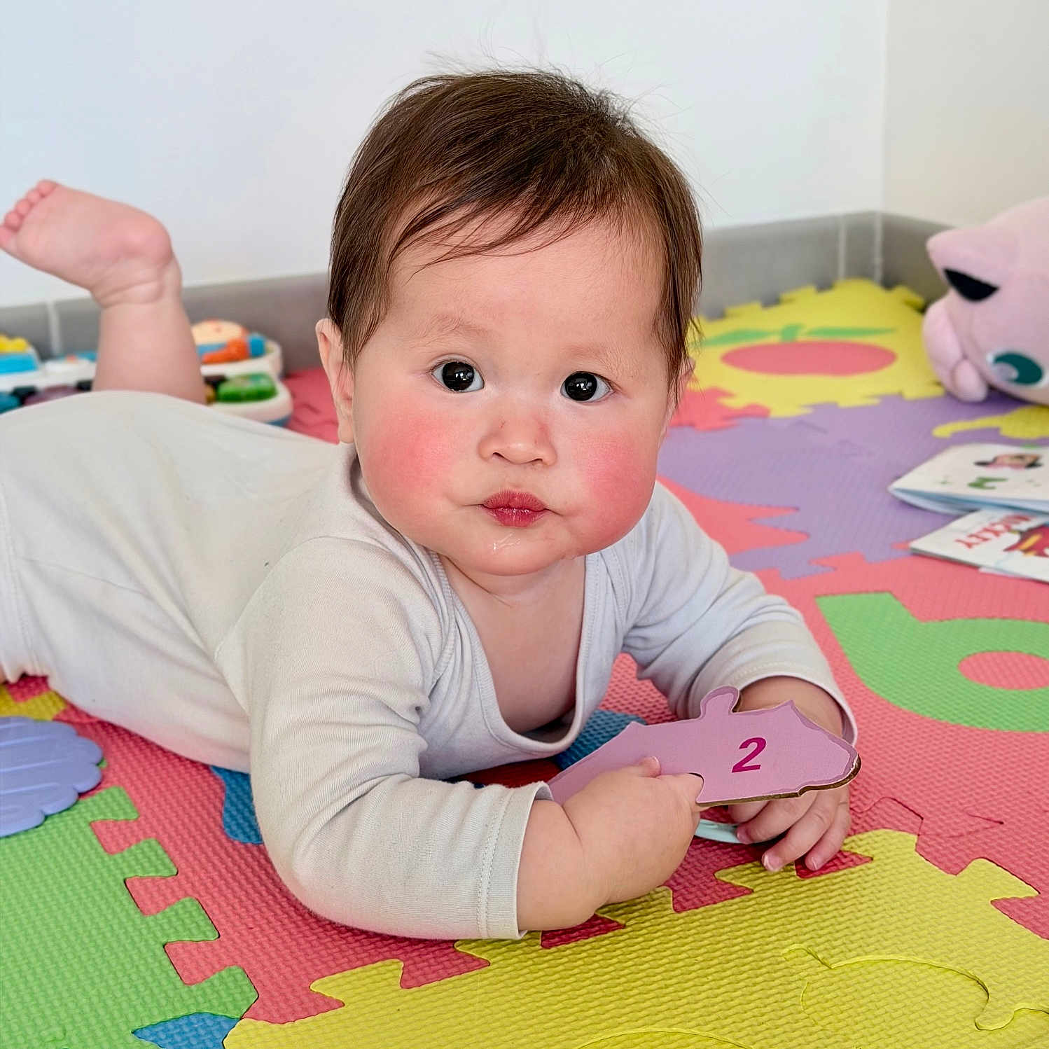 Léna a rejoint le concours — aidez-le/la à gagner de superbes lots ! baby, child, infant, puzzle_piece, number_two, foam_mat, colorful, toy, book, floor, indoors, cute, curious, face, hand, playing, lying_down, cheeks, clothing, person