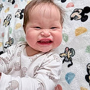 Léna a rejoint le concours — aidez-le/la à gagner de superbes lots ! baby, child, face, expression, scrunched_face, onesie, animal_print, blanket, mickey_mouse, pattern, cute, funny, infant, smile, chubby_cheeks, lying_down, indoors, soft_toy_pattern, happy, person