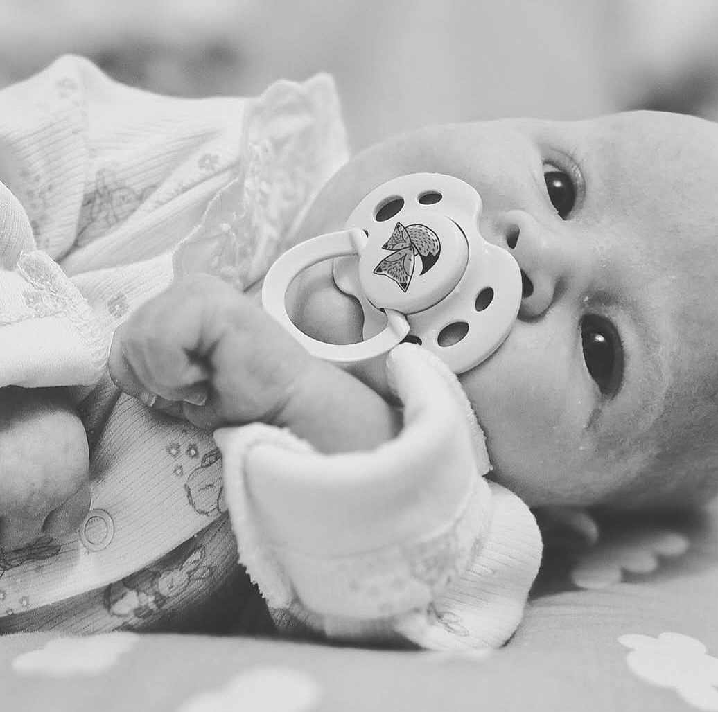 Aria joined the competition — help win amazing prizes! baby, pacifier, close_up, black_and_white, infant, onesie, cute, newborn, face, hand, sleeping_area, soft, child, portrait, lying_down, expression, young, peaceful, indoors, cozy