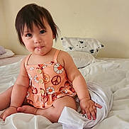 Adriana joined the competition — help win amazing prizes! toddler, child, baby, bed, blanket, pillow, dress, orange, peace_sign, flower_pattern, drool, hair, skin, indoor, sitting, cute, looking, hand, foot, white