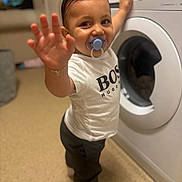 Teddie Lee joined the competition — help win amazing prizes! toddler, child, pacifier, washing_machine, white_tshirt, black_pants, indoor, home, flooring, smiling, hand, person, young_child, clothing, hair, appliance, playful, standing, household, curious