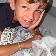 Aarôn participe au concours pour gagner de l'argent avec cette photo : child, boy, smiling, bed, blanket, pillow, plush_toy, bracelet, casual_clothing, indoors, portrait, young, happy, face, head, hand, resting, cozy, relaxed, home
