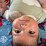 Mateo is registered to the contest to win money with this photo: baby, infant, child, face, eyes, smile, clothing, onesie, blanket, pattern, holiday, christmas, snowflake, red, green, blue, skin, head, hair, lying_down
